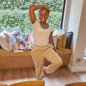 Young black girl balancing on one foot with one hand on head in Girl-School class.